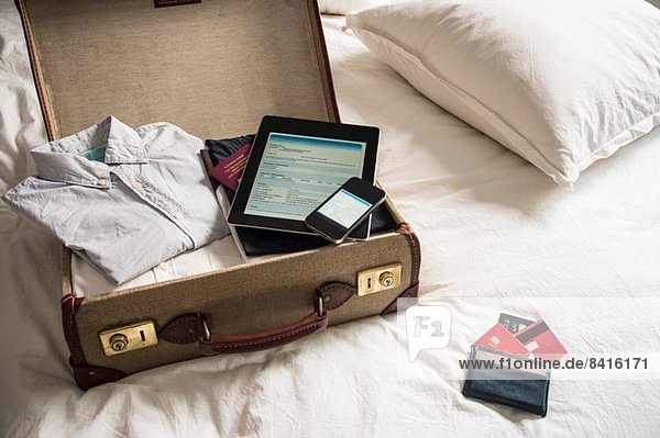 Offener Koffer auf dem Bett mit digitalem Tablett und Handy