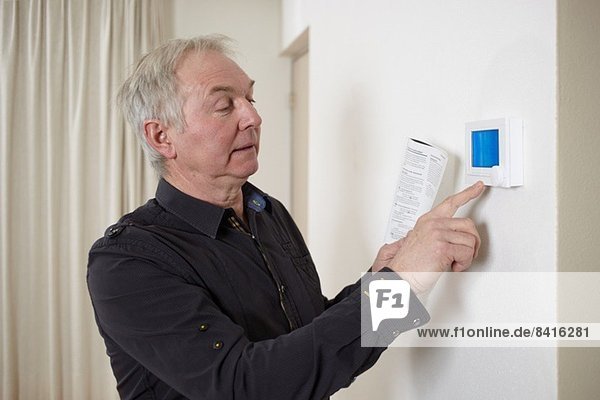Senior man at home adjusting heating control panel
