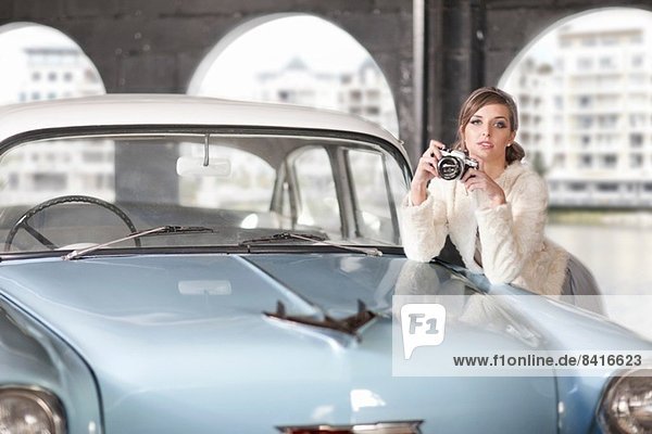 Woman leaning on convertible holding camera