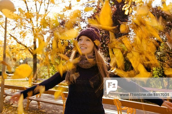 Young woman throwing up autumn leaves in park