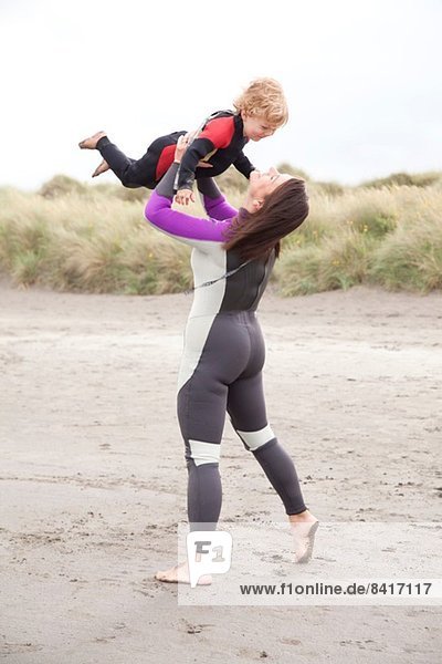 Mother lifting son on beach