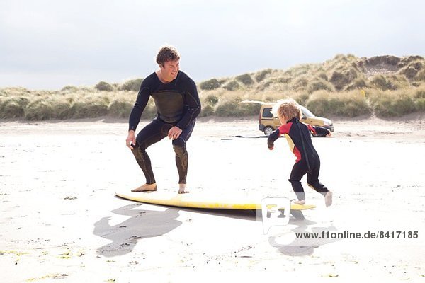 Vater und Sohn mit Surfbrett am Strand