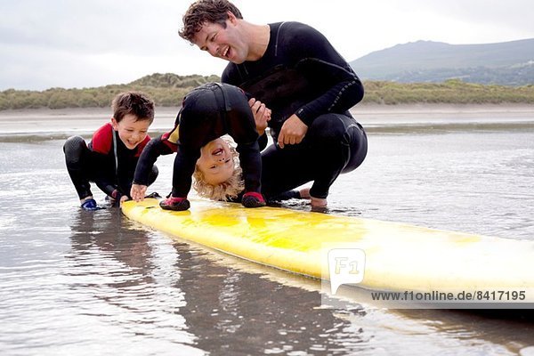 Vater und Söhne spielen mit dem Surfbrett