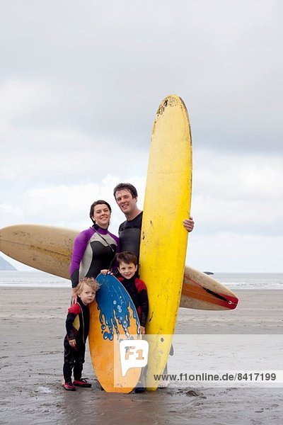 Familienporträt mit zwei Jungen mit Surfbrettern am Strand