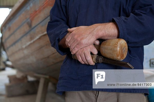 Nahaufnahme von Schreinerhänden mit Meißel in der Bootswerkstatt