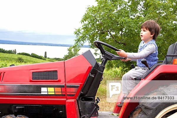Männliches Kleinkind  das vorgibt  einen Traktor im Garten zu fahren.