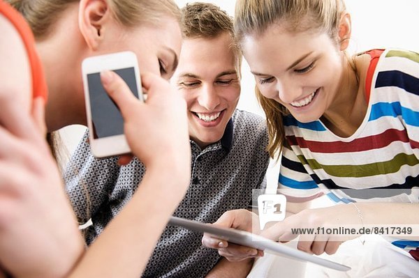 Drei junge erwachsene Freunde beim Betrachten des digitalen Tabletts