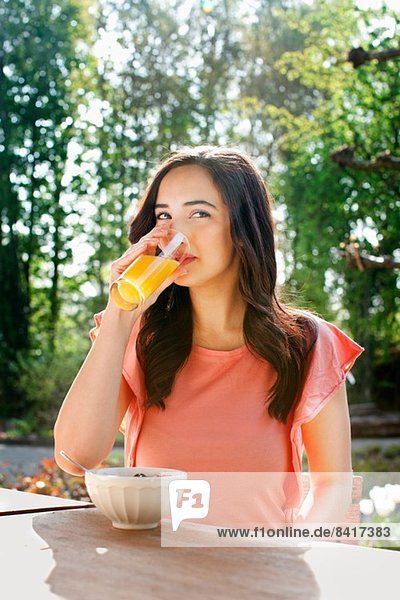Portrait of young woman drinking orange juice in garden