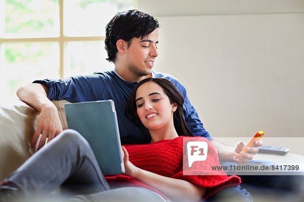 Junges Paar mit digitalem Tablett und Mobile auf dem Wohnzimmersofa