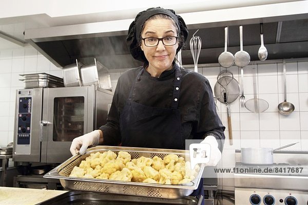 Woman working in restaurant kitchen  holding tray of cauliflower