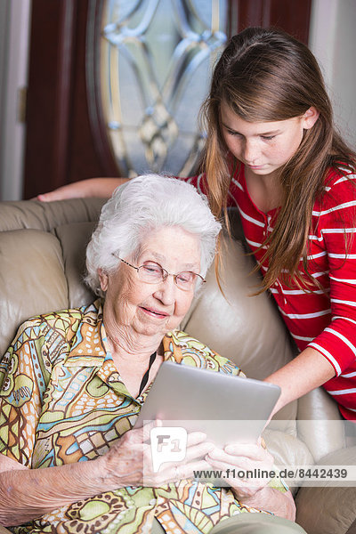 Aged woman and her great-granddaughter looking at tablet computer