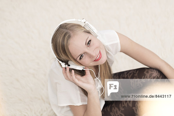 Lächelnde junge Frau mit Kopfhörern auf einem Teppich sitzend