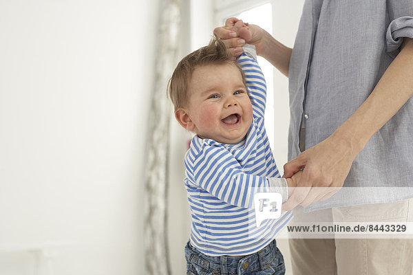 Lachender Babyjunge Hand in Hand mit seiner Mutter