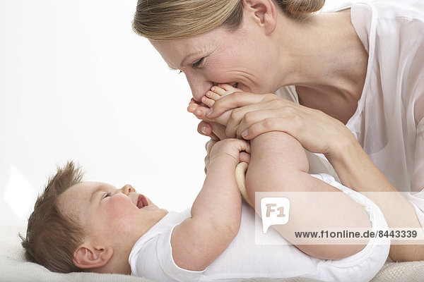 Mutter küsst die Füße ihres lächelnden Babyjungen