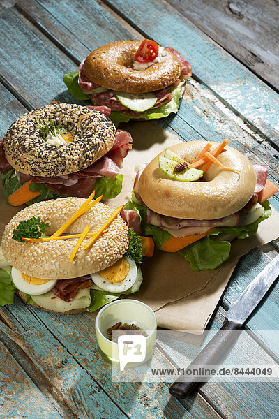 Four different bagels garnished with salami  slices of bacon  rocket salad  tomato  lettuce  cucumber carrot  egg  cream cheese and cress and parsley
