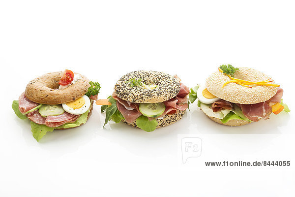 Drei verschiedene Bagels  garniert mit Salami  Speckscheiben  Rucola  Tomate  Salat  Gurkenmöhre  Ei  Frischkäse und Kresse und Petersilie.