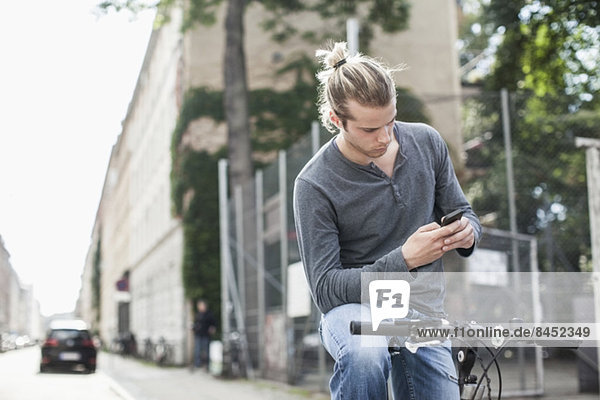 Junger Mann SMS über Handy beim Sitzen auf dem Fahrrad auf der Straße
