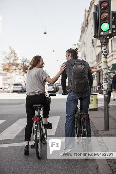 Rear view of couple with bicycles waiting on zebra crossing at city street