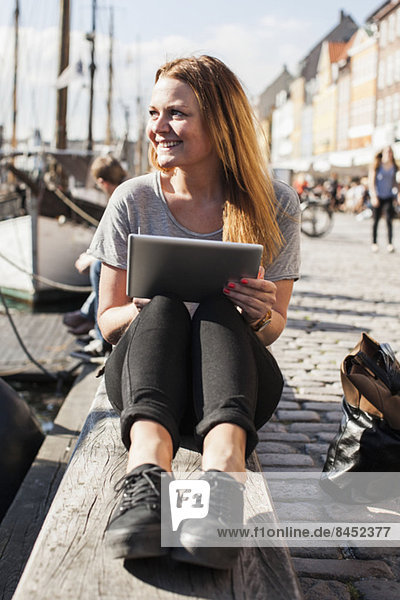 Glückliche Frau mit digitalem Tablett im Hafen sitzend