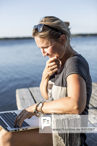 Mittlere erwachsene Frau lächelt bei der Benutzung des Laptops am Pier