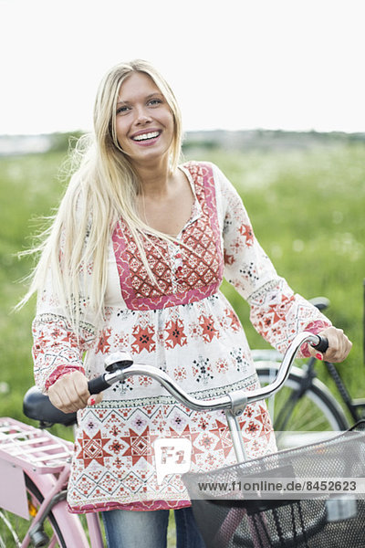 Bildnis einer glücklichen jungen Frau mit Fahrrad auf dem Feld
