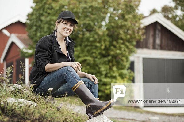 Vollständiges Porträt einer selbstbewussten Bäuerin  die auf einem Felsen auf dem Bauernhof sitzt.