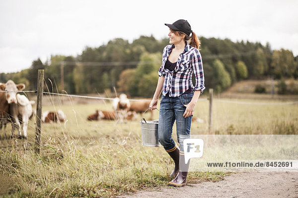 Female farmer with bucket walking while animals grazing in field