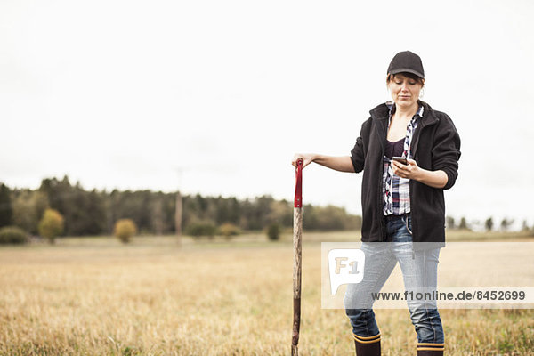 Mittlere erwachsene Bäuerin mit Handy im Feld