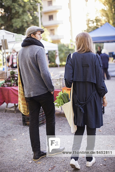 Rear view of young couple with leafy vegetables at market
