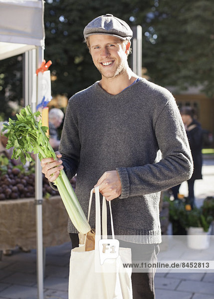 Portrait of happy man holding celery in market