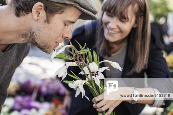 Young man smelling flowers held by woman in market
