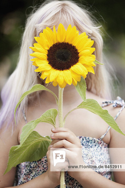 Mädchen mit Sonnenblume vor dem Gesicht im Freien