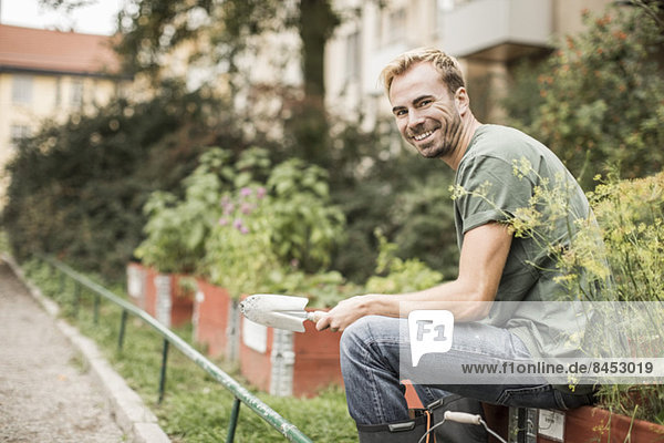 Seitenansicht Porträt eines glücklichen Mannes mit Schaufel im Garten sitzend