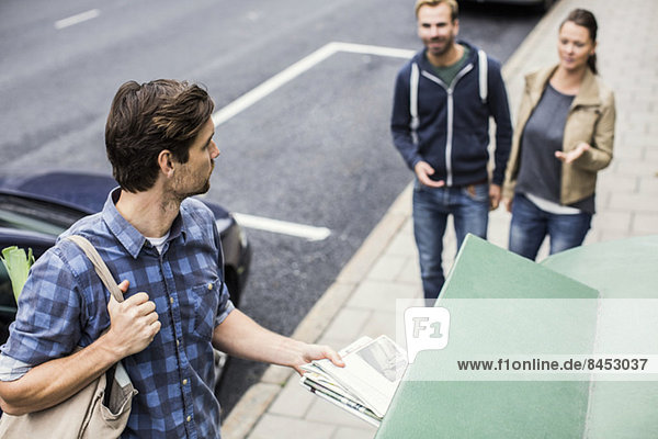 Mann  der Zeitung in den Papierkorb legt  während er Freunde auf dem Bürgersteig betrachtet