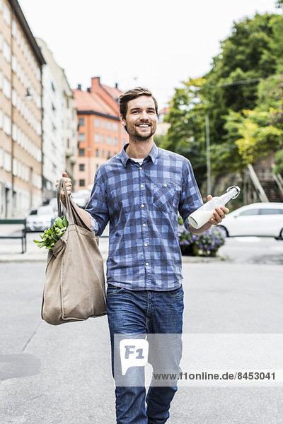 Full length portrait of happy man with groceries walking on street