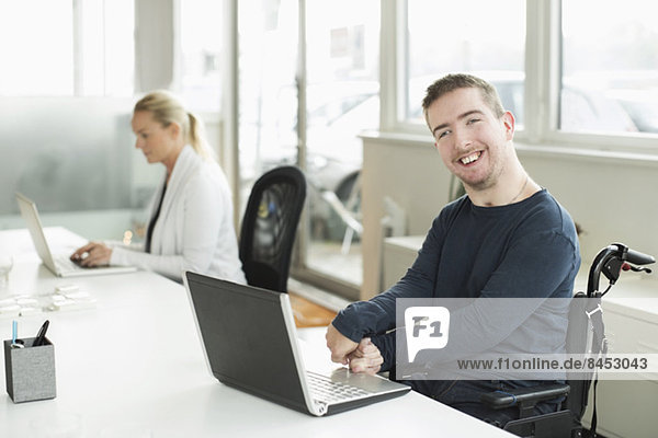 Portrait eines glücklichen Geschäftsmannes mit zerebraler Lähmung mit Laptop im Büro