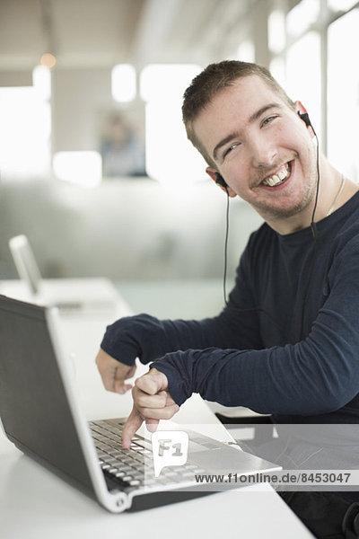 Portrait of happy businessman with cerebral palsy using laptop while listening music