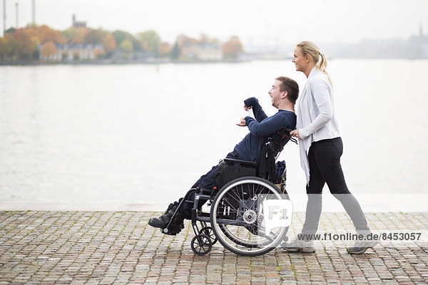 Caretaker pushing disabled man on wheelchair along lake