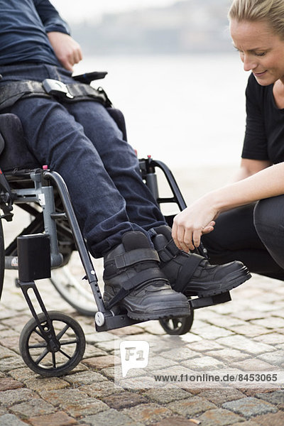 Hausmeisterin beim Anziehen von Behindertenschuhen im Freien