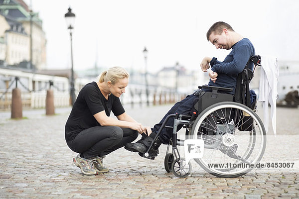 Hausmeisterin beim Anziehen von Behindertenschuhen auf der Straße