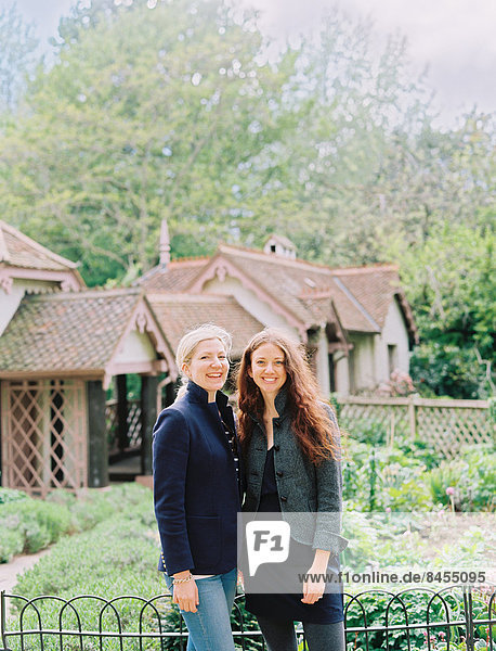 Two women standing in a garden of a historic house.