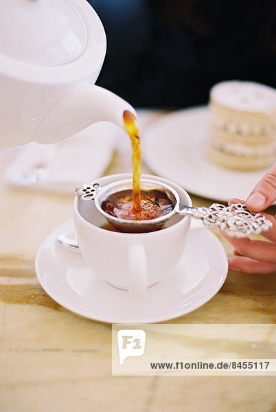 A person pouring a cup of tea  using a strainer. White china. Elegant afternoon tea.