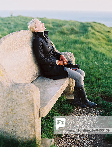 Eine Frau saß auf einer Steinbank an einem Küstenweg.