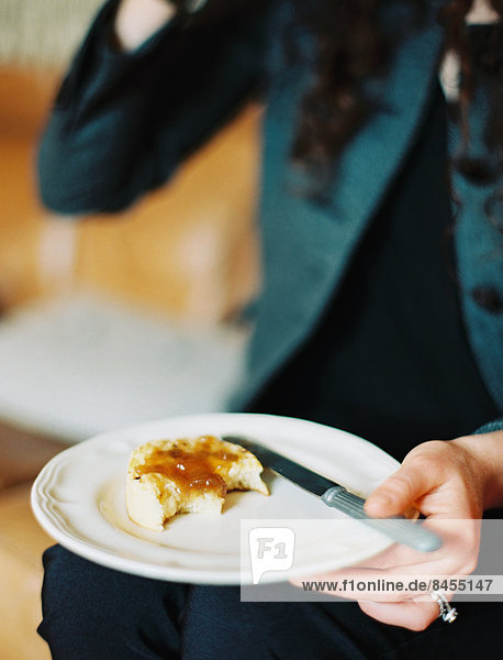 A person holding a plate  holding a half eaten scone with jam.