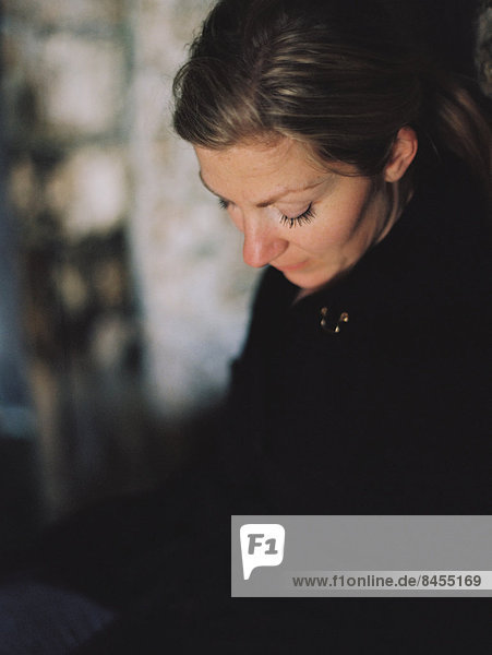 A woman wearing a black coat  looking down in a pensive mood.