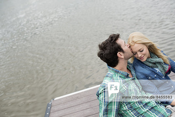 Ein Mann und eine Frau sitzen auf einem Steg an einem See.