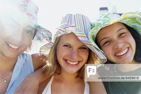 Drei junge Mädchen in einer Reihe mit Sonnenhüten  die in die Kamera blicken und lächeln.