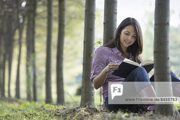 Eine Frau sitzt unter den Bäumen und liest ein Buch.