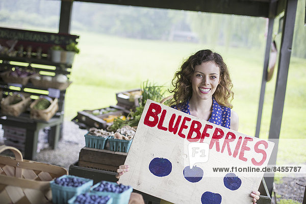 An organic fruit and vegetable farm. A person carrying a blueberries sign.