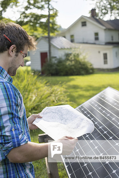 Ein Mann  der einen Plan zur Anbringung einer Solaranlage im Garten eines Bauernhauses verwendet.